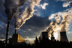 A view of the smoking chimneys of a coal-fired power plant against the backdrop of a dramatic sky with clouds.