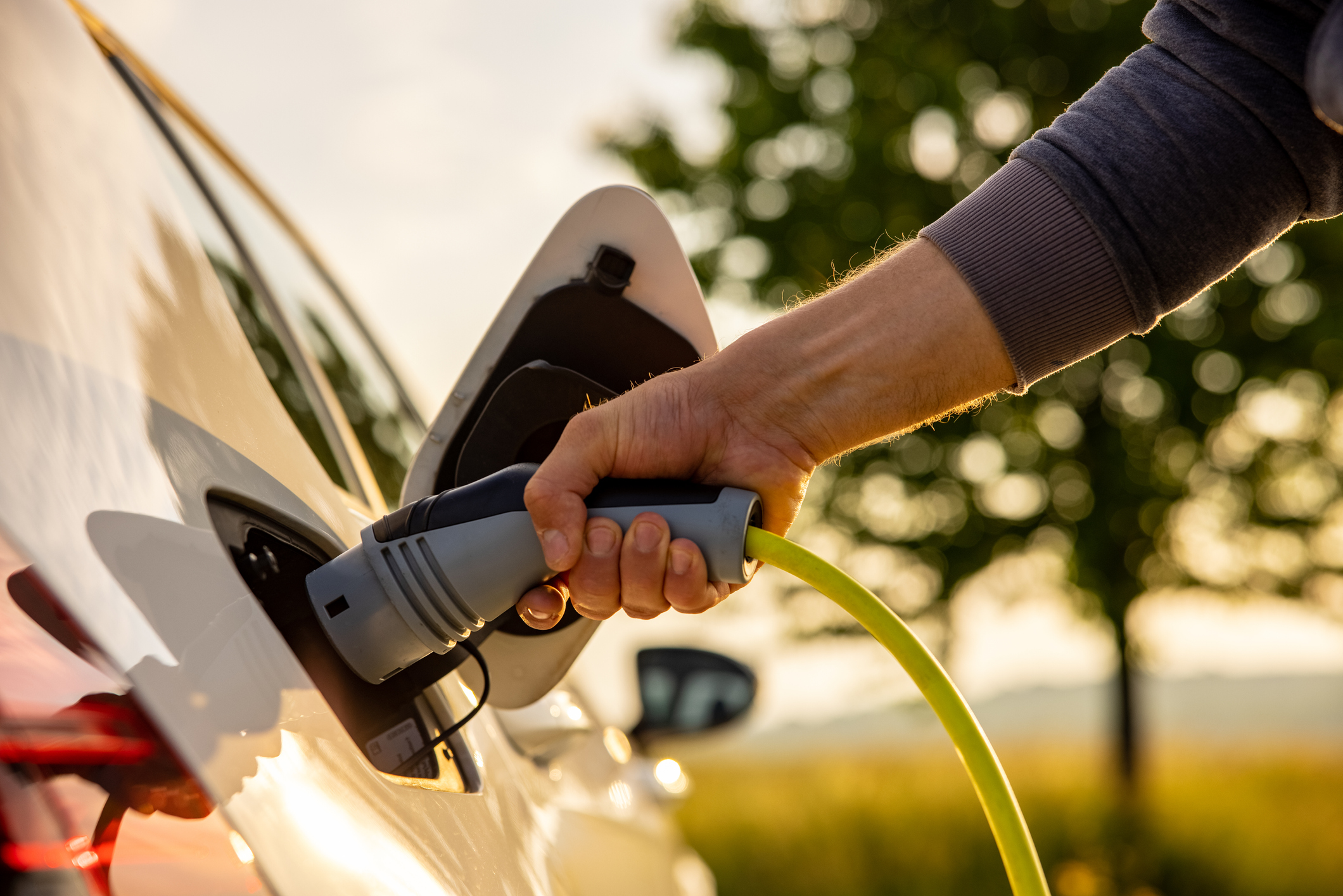 Man inserts a power cord into an electric car for charging