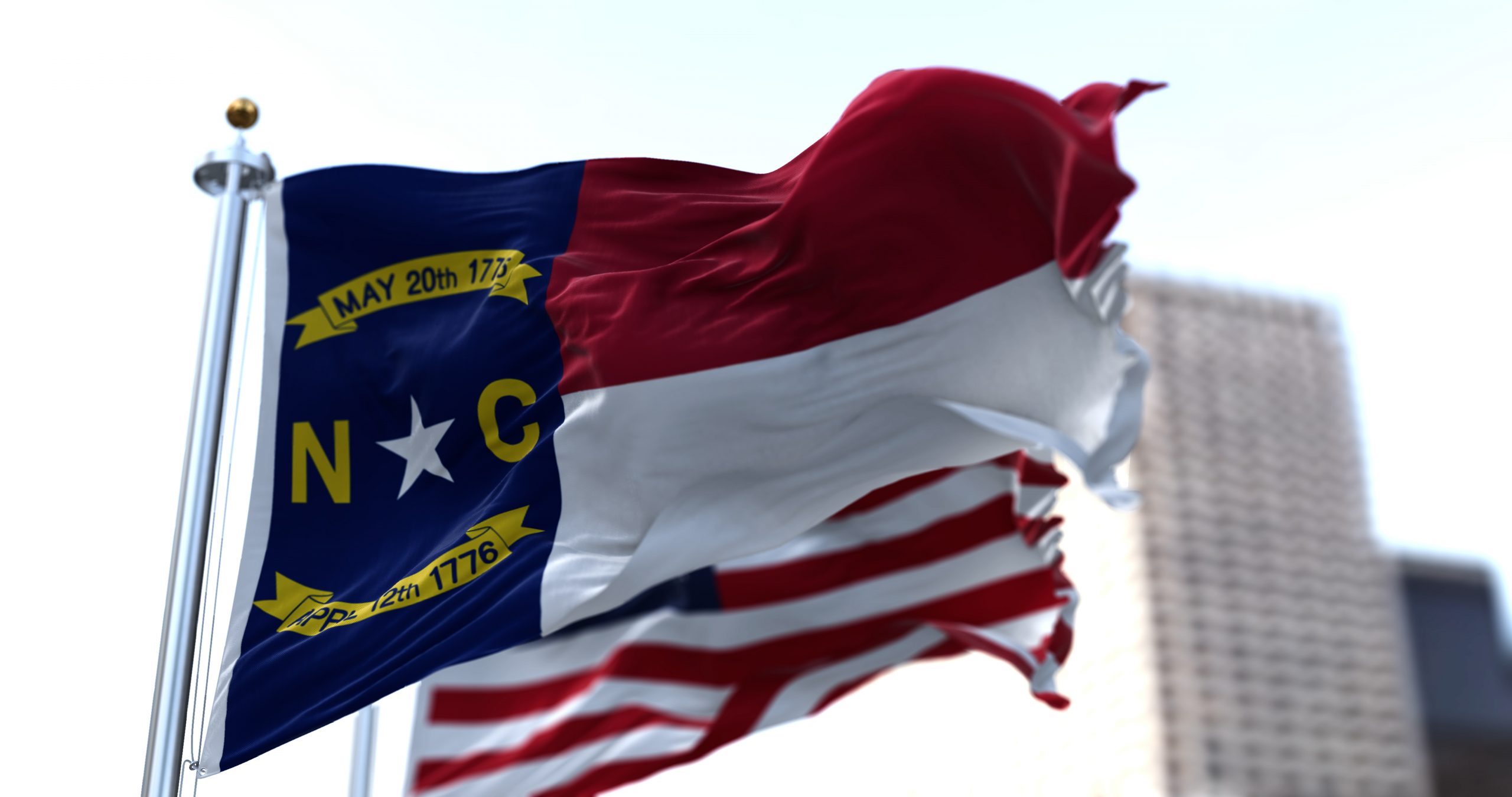 The flags of the North Carolina state and United States of America waving in the wind. Democracy and independence.