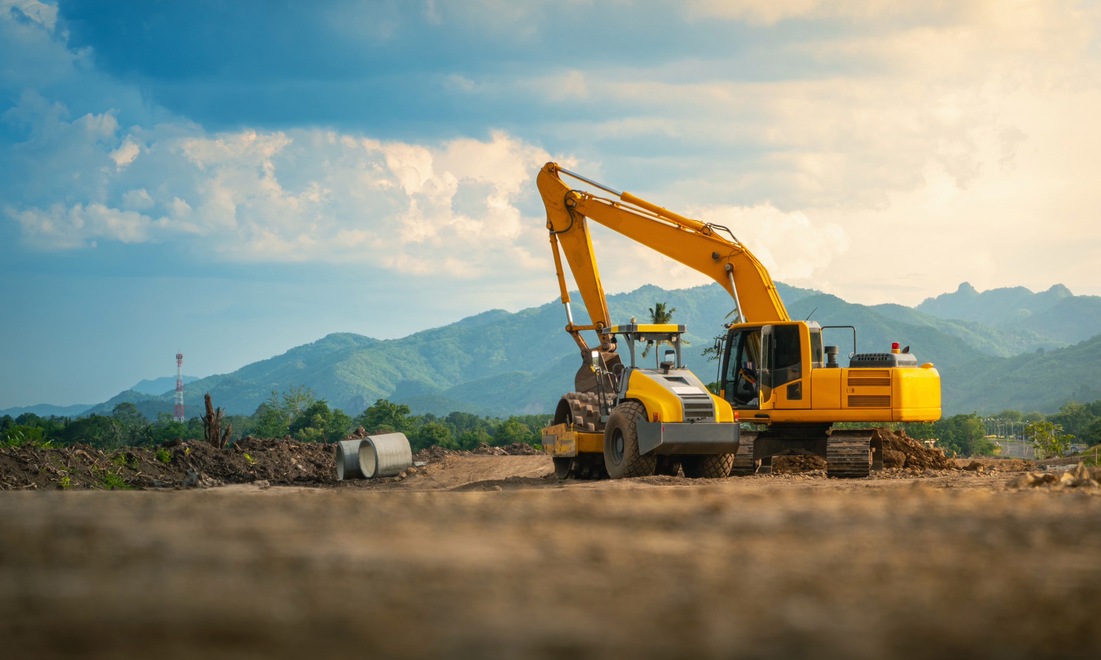 Backhoe working in road construction site, with mountains and sky background.