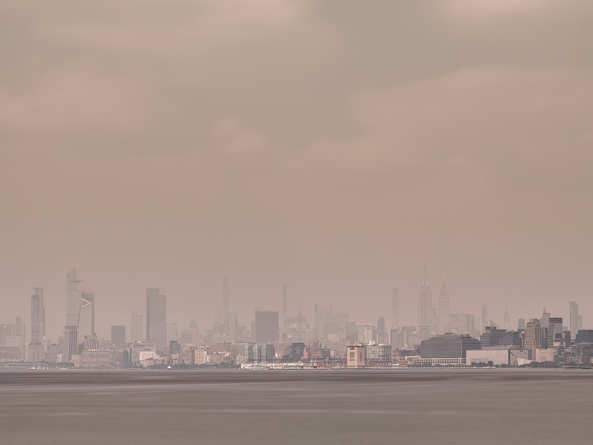 Long exposure of Hudson Yards and Midtown Manhattan across the Hudson River on a hazy day where the Canadian fire smoke engulfs the city including the Empire State Building and the Chrysler Building