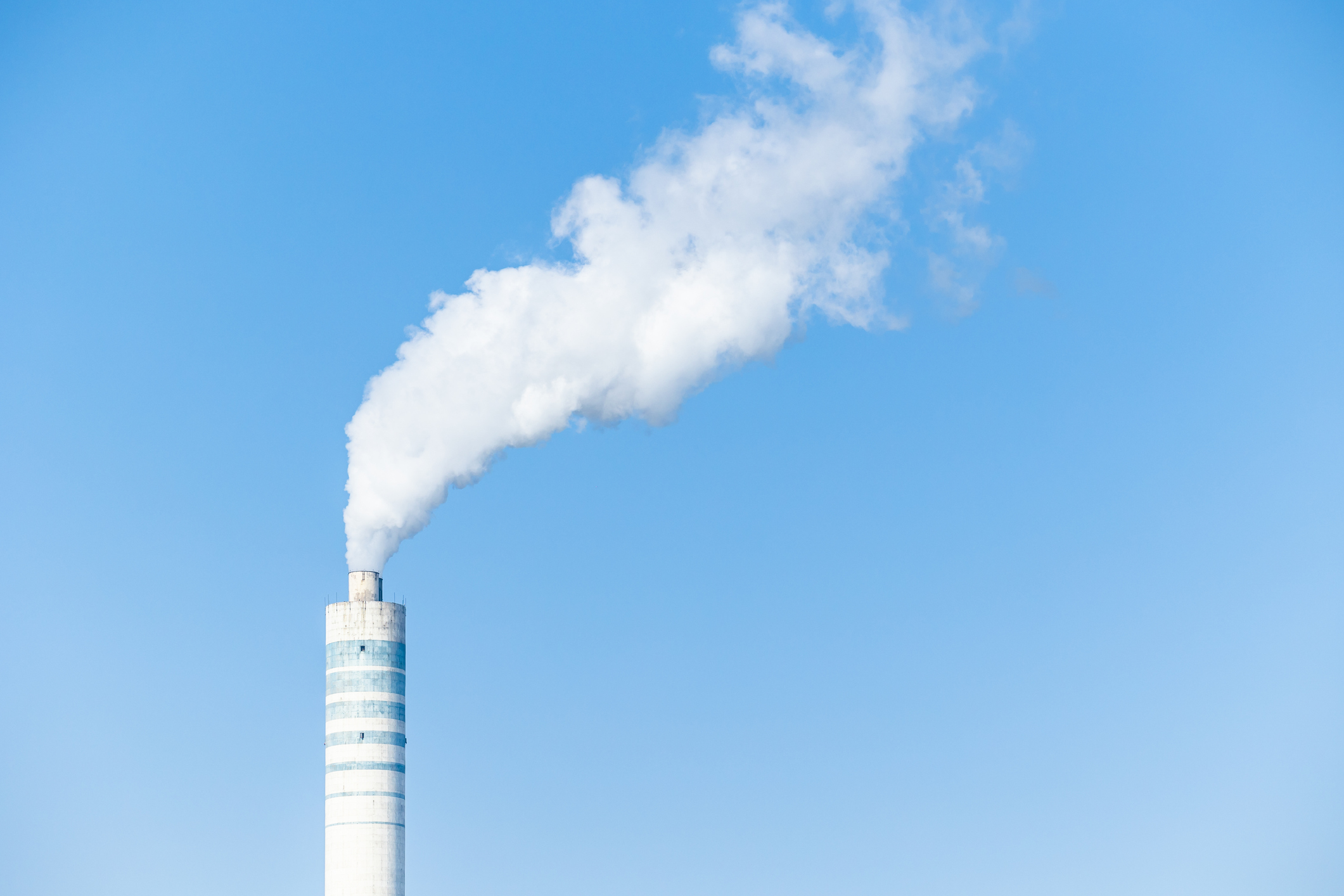 Industry chimney with white smoke stack against blue sky.