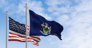 Maine state flags and the American flag waving in the wind on a clear day