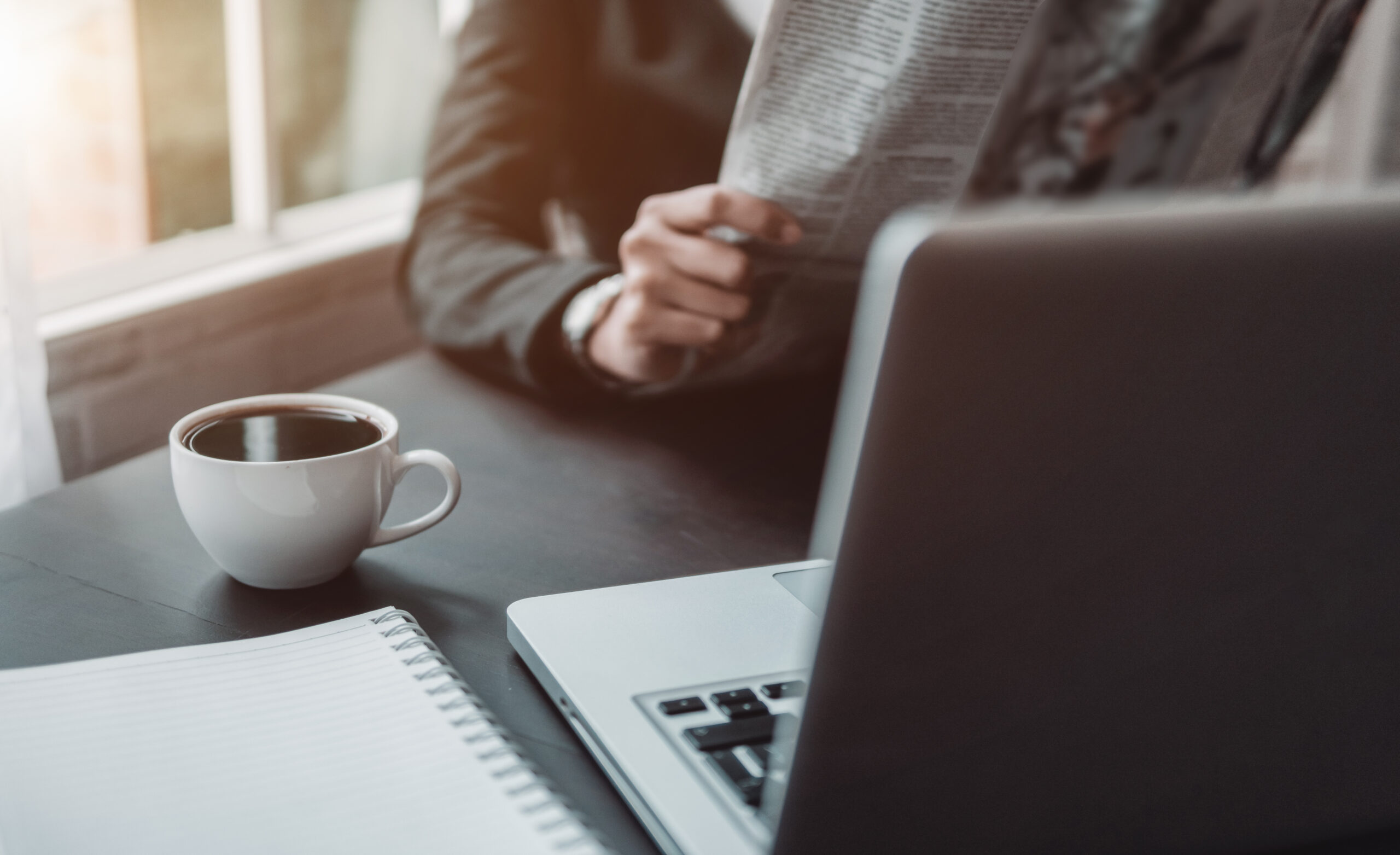 business professional reading a newspaper in office with coffee cup.