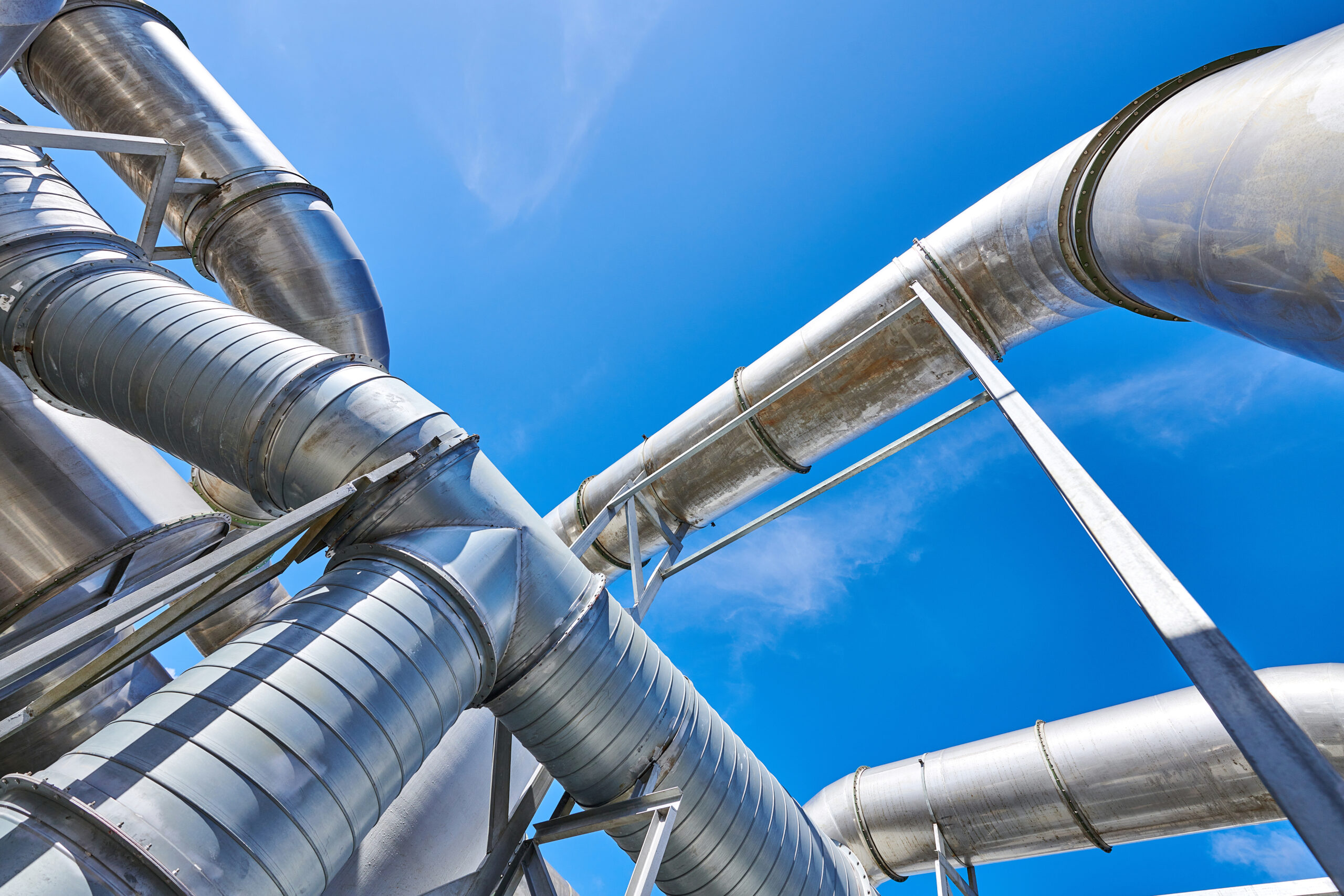 Low angle view of silver colored transport pipelines at blue sky.
